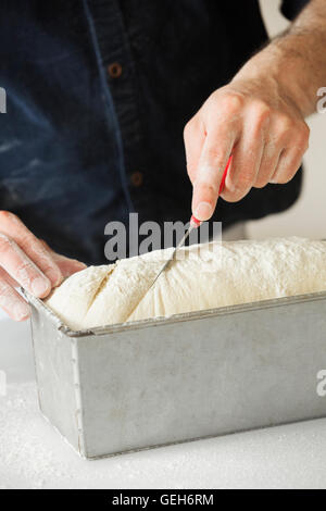 Close up of a baker cutting bread dough in a baking tin. Stock Photo