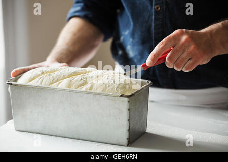 Close up of a baker cutting bread dough in a baking tin. Stock Photo