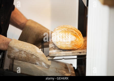 Close up of a baker taking a freshly baked loaf bread out of an oven. Stock Photo