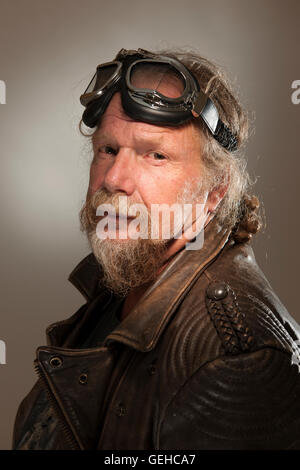 side head and shoulders portrait of older man with a full beard, leather jacket and goggles seriously into the camera Stock Photo