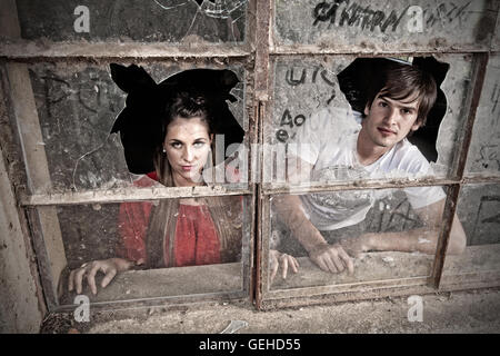 Man and a woman looking out through a window with broken glass Stock Photo