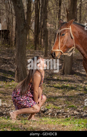 Girl kneeling down with funny face looking up at a horse Stock Photo