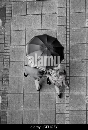 Couple sharing the umbrella while walking down the wet sidewalk in the center in black and white Stock Photo
