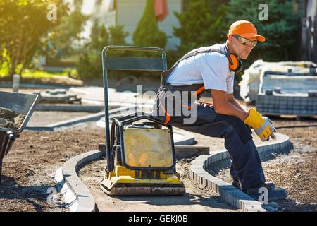 Brick Paver Worker Resting on His Soil Plate Compactor While at Work. Stock Photo