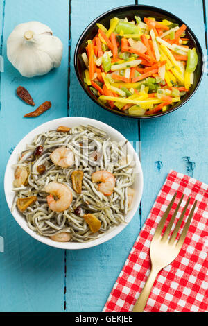 Surimi elvers with prawns, garlic and pepper on a white bowl, and vegetables on a black bowl Stock Photo