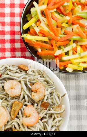 Surimi elvers with prawns, garlic and pepper on a white bowl and vegetables on a black bowl Stock Photo