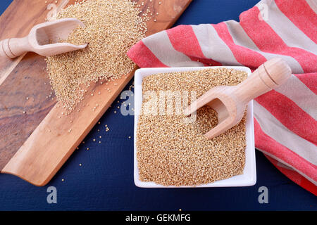 White grain quinoa with wooden scoops and chopping board on dark blue wood background. Stock Photo