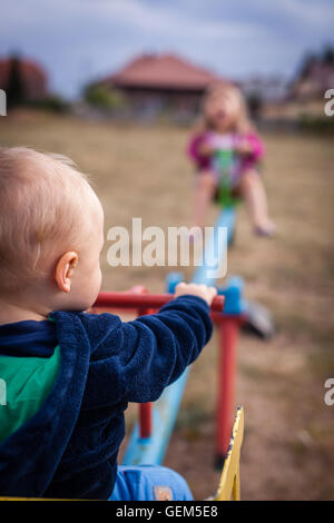 Little boy and his sister having fun on a swing in an outdoor playground Stock Photo