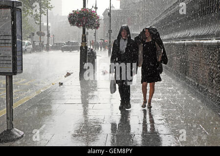 People couple man woman with raincoats walking in heavy pouring rain in wet summer on a city street in Charing Cross, London England UK  KATHY DEWITT Stock Photo