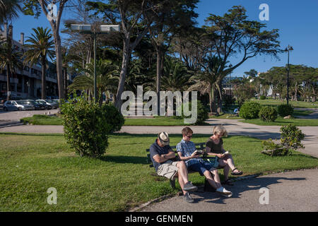 Sleeping man with a reading young man and lady, on a park bench at Estoril near Lisbon, Portugal. Stock Photo