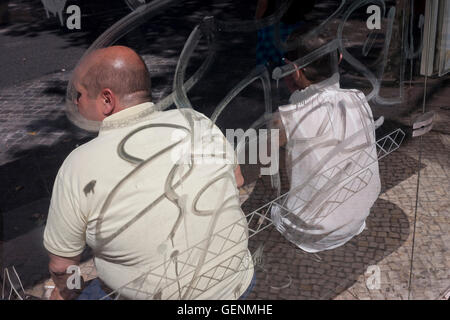 Squiggles and lines cast shadows over the backs of two passengers awaiting their bus outside Apolonia station in Lisbon Stock Photo