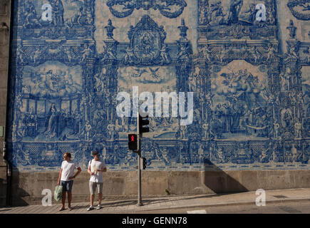 Two young wait to cross the road beneath traditional Azulejo tiles on the wall of Capela Das Almas (church), Porto Stock Photo