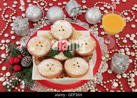 Christmas mince pie cakes with eggnog drink, silver bauble decorations, holly and winter greenery on red background. Stock Photo