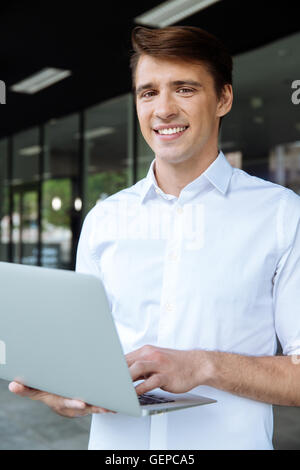 Smiling young businessman standing and working with laptop Stock Photo