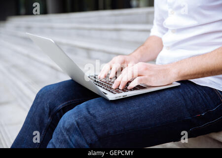 Closeup of young man sitting on stairs and using laptop Stock Photo