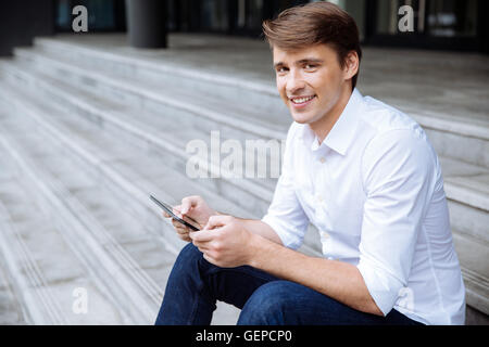 Happy young man sitting on stairs and using tablet outdoors Stock Photo