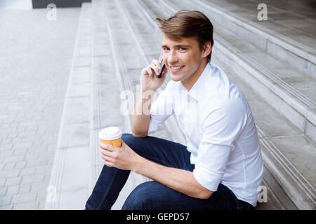 Smiling young businessman drinking coffee and talking on cell phone outdors Stock Photo