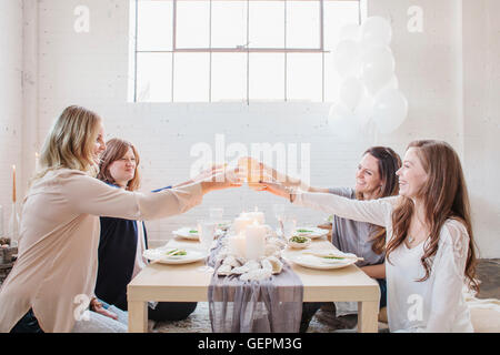 Four women seated at a low table, raising their glasses in a toast to each other. Stock Photo