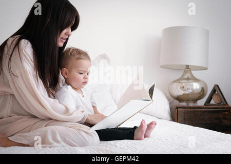 A heavily pregnant woman playing with her young son. Sitting on a bed, reading a story. Stock Photo