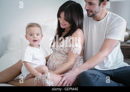 A young couple and their young son sitting together on their bed. Stock Photo