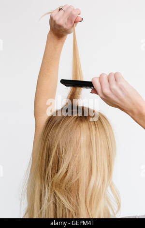 A young woman with long blond wavy hair using a comb. Back view. Stock Photo