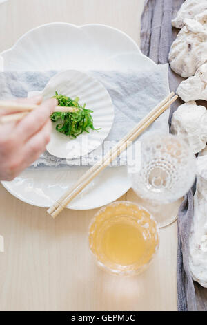 Overhead view of a table and a woman using chopsticks to eat vegetables. Stock Photo