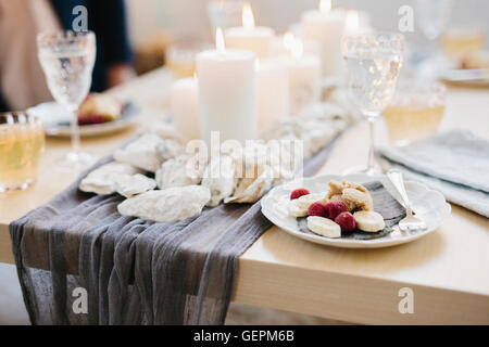 A table for a celebration meal with wine glasses filled and plates of fruit, and lit candles in the centre of the table. Stock Photo