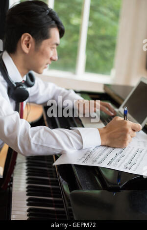 Young man sitting at a grand piano in a rehearsal studio, annotating sheet music. Stock Photo