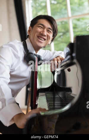 Young smiling man sitting at a grand piano in a rehearsal studio, wearing headphones round his neck. Stock Photo