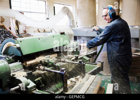 Man standing in a carpentry workshop, wearing hearing protectors, working at a woodworking machine. Stock Photo