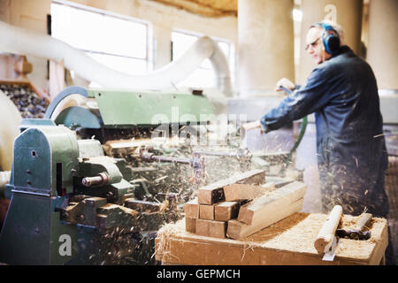 Man standing in a carpentry workshop, wearing hearing protectors, working at a woodworking machine. Stock Photo