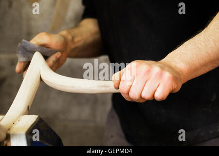 Close up of a man sanding a piece of curved wood in a carpentry workshop. Stock Photo