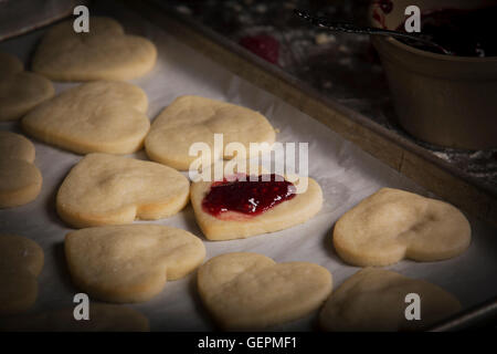 Valentine's Day baking, close up of a baking tray with heart shaped biscuits and raspberry jam. Stock Photo