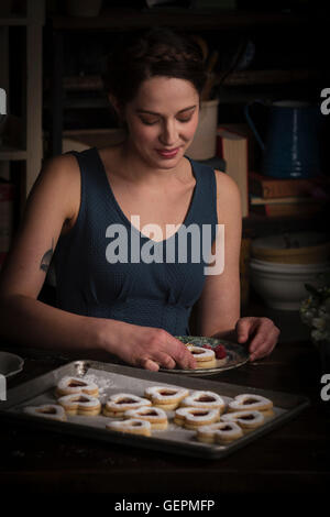 Valentine's Day baking, young woman sitting in a kitchen, with a baking tray of heart shaped biscuit. Stock Photo