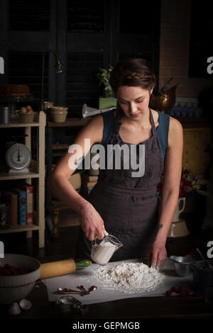 Valentine's Day baking, young woman standing in a kitchen, preparing dough for biscuits, pouring milk from a jug. Stock Photo