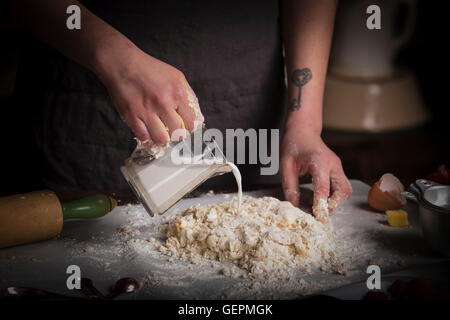 Valentine's Day baking, woman preparing dough for biscuits, pouring milk from a jug. Stock Photo