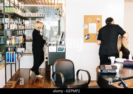 A hair stylist working on a client's hair, and a woman on the telephone, looking at a laptop computer. Stock Photo