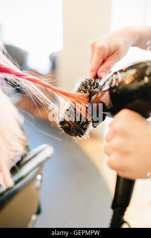 A hair stylist blow-drying a client's long straight pink hair using a round bristle brush. Stock Photo
