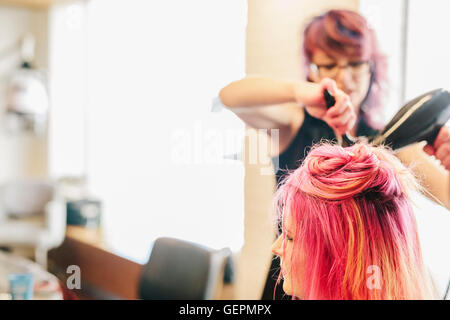 A hair stylist blow-drying a client's long pink dyed hair. Stock Photo