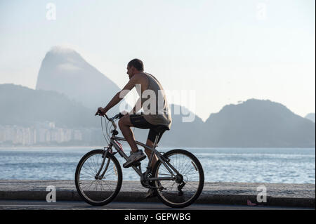 RIO DE JANEIRO - APRIL 3, 2016: Young Brazilian man rides a bicycle on the beachfront boardwalk at Copacabana Beach. Stock Photo