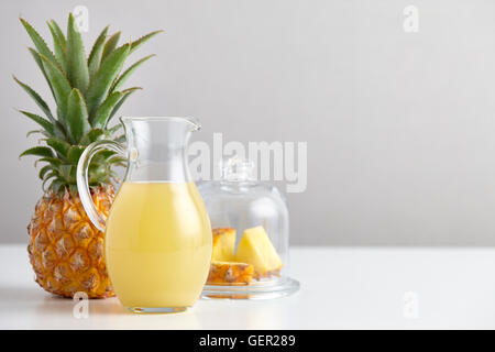 Glass jug with pineapple juice and fruit on table Stock Photo