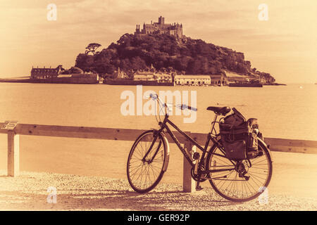 Bicycle leaned on a wooden barrier on a promenade on a coast of Marazion with the St Michaels Mount in the background, Cornwall, Stock Photo