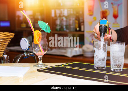 Empty glass from cocktail with umbrella, straw and orange slice is the bar in cafe. Bartender pours soda into glasses with ice Stock Photo