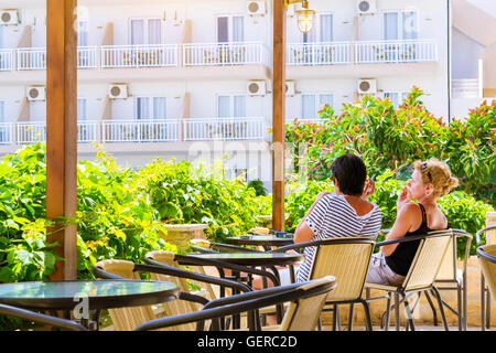 BALI, GREECE - APRIL 29, 2016: Two adult females smoke, sitting on chairs on the terrace, surrounded by decorative green plants Stock Photo