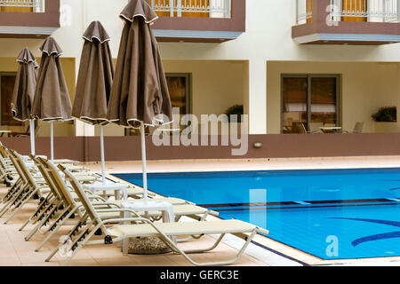 Empty sunbeds and umbrellas are at the pool empty without tourists early in the morning. Relax and sunbathe by pool, Crete Stock Photo