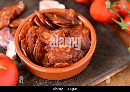 closeup of an earthenware bowl with some slices of Spanish chorizo, a pork sausage typical of Spain, on a rustic wooden table wi Stock Photo
