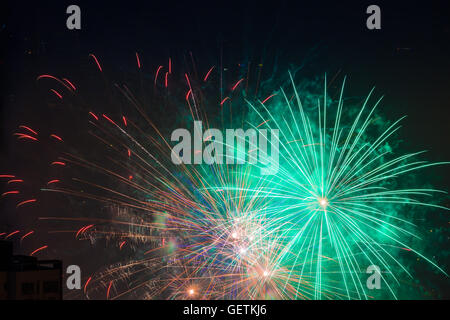 Multiple green orange fireworks burst above buildings Stock Photo