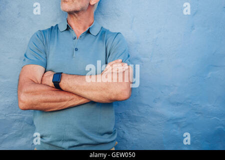 Cropped shot of mature man wearing smart watch against blue background. Middle aged man standing with his arms crossed against a Stock Photo