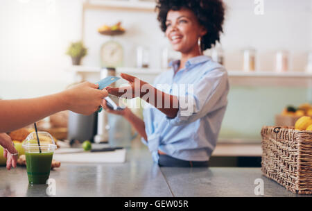Cropped shot of female employee taking payment from customer, focus on female hands giving credit card for juice bar payment. Stock Photo