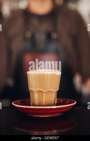 Shot of cup of coffee with saucer on cafe counter with barista standing in background. Stock Photo